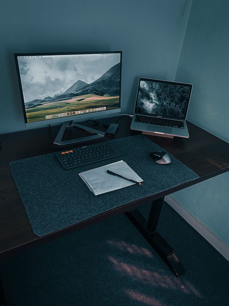 Bureau assis-debout avec écran et ordinateur portable, ambiance sombre et feutrée