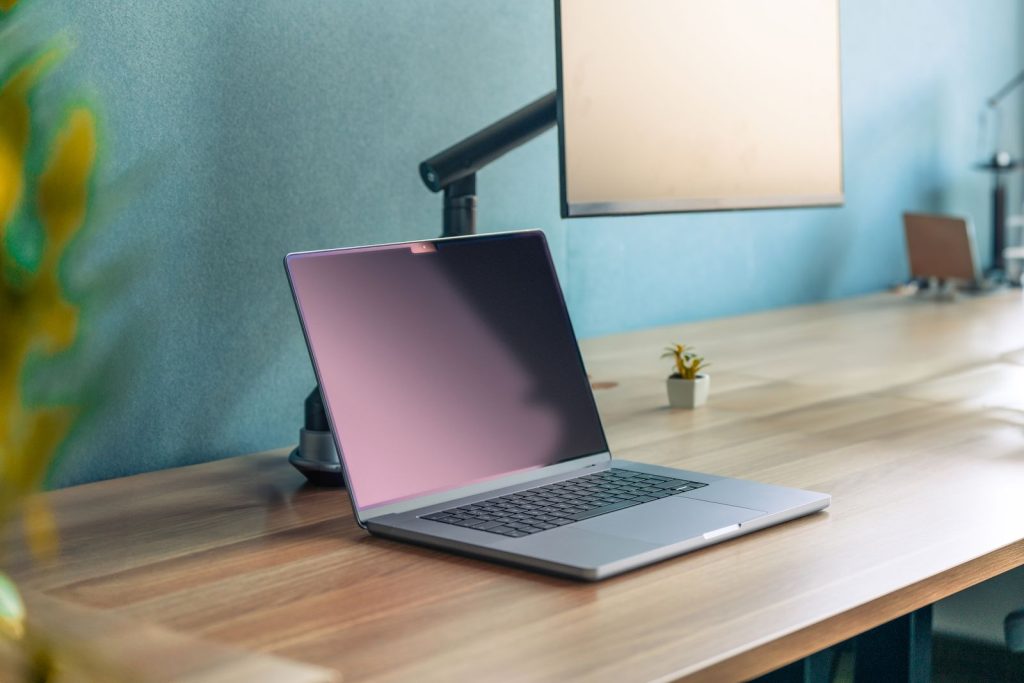Écran tenu par un bras articulé au-dessus d'un ordinateur portable posé sur un bureau en bois