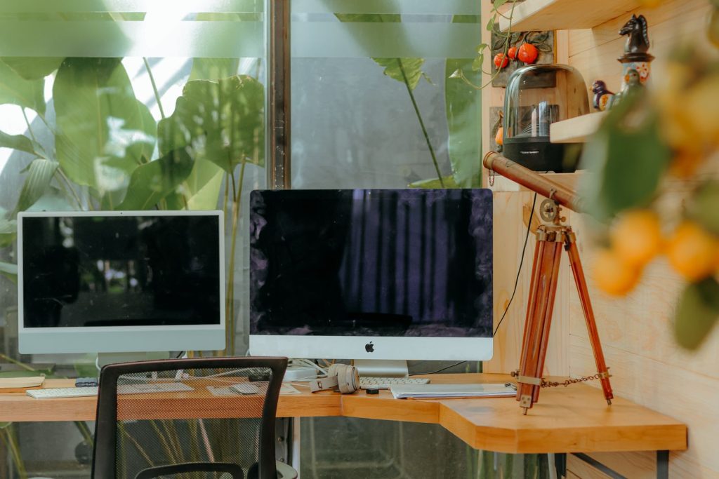 Bureau d'angle en bois clair logé dans un coin de pièce, avec deux écrans