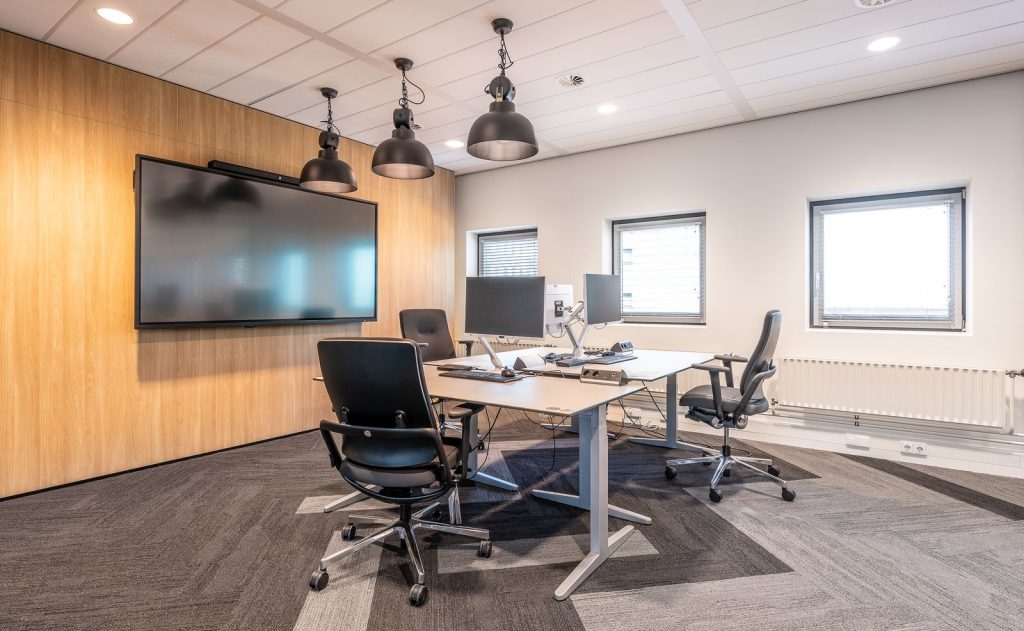 Salle de travail avec des bureaux réglables à piètement blanc, des écrans et des fauteuils