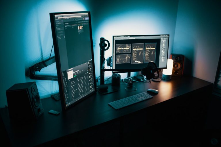 Bureau sombre et dégagé avec un écran vertical et un écran horizontal sur bras articulés, éclairage d'ambiance bleu