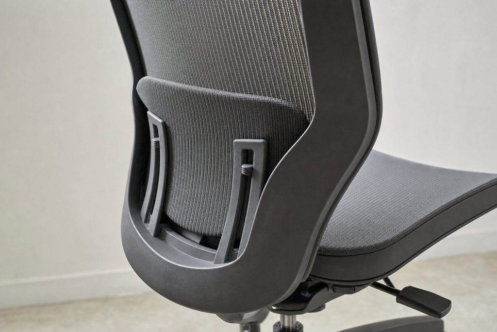 Vue arrière d'un dossier de chaise ergonomique en maille grise avec un coussin lombaire séparé monté sur des glissières verticales