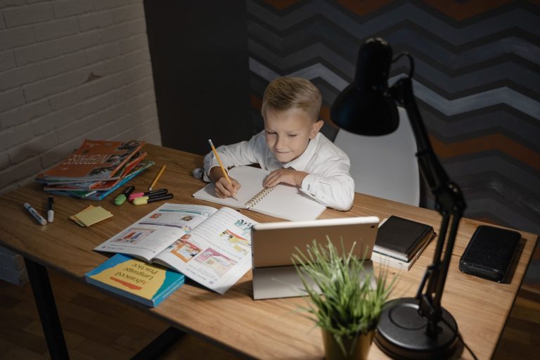 Enfant qui fait ses devoirs à un bureau en bois, sous une lampe articulée