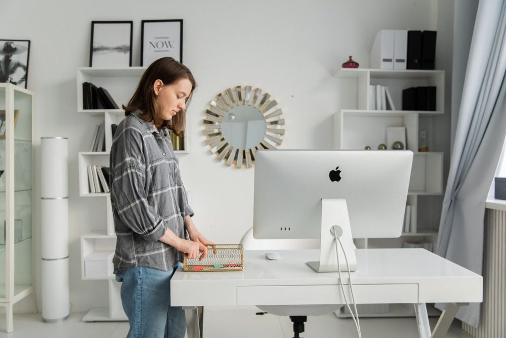 Femme debout devant un bureau blanc relevé, avec un ordinateur, dans une pièce lumineuse