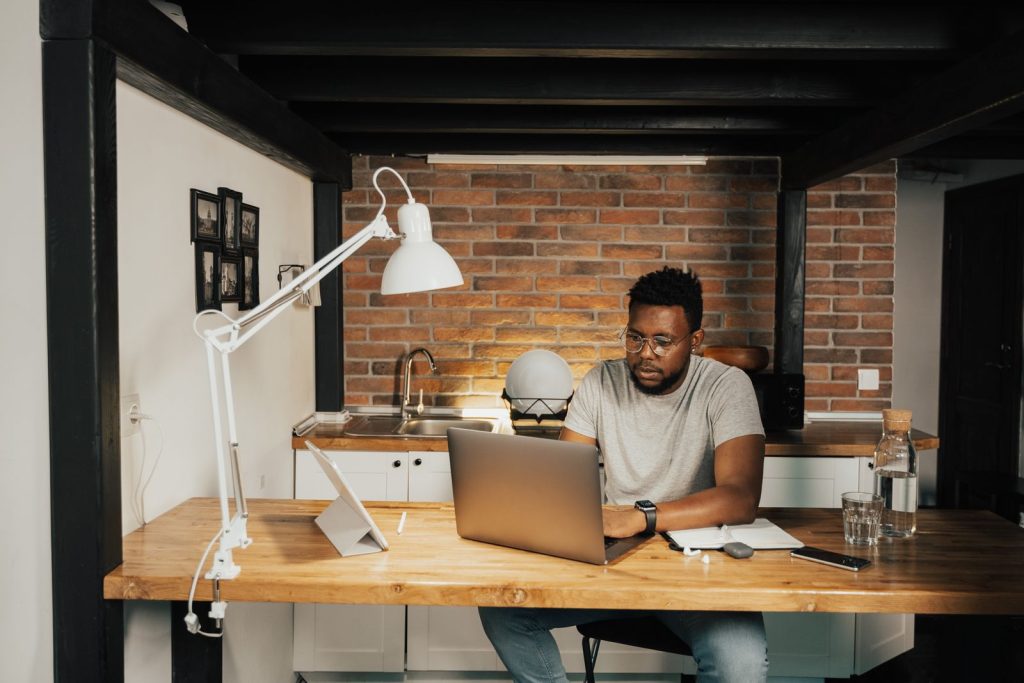 Homme travaillant sur un ordinateur portable à un grand bureau en bois, sous une lampe d'architecte
