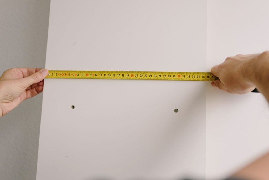 Deux mains tendent un mètre ruban jaune le long d'un mur, près de l'angle