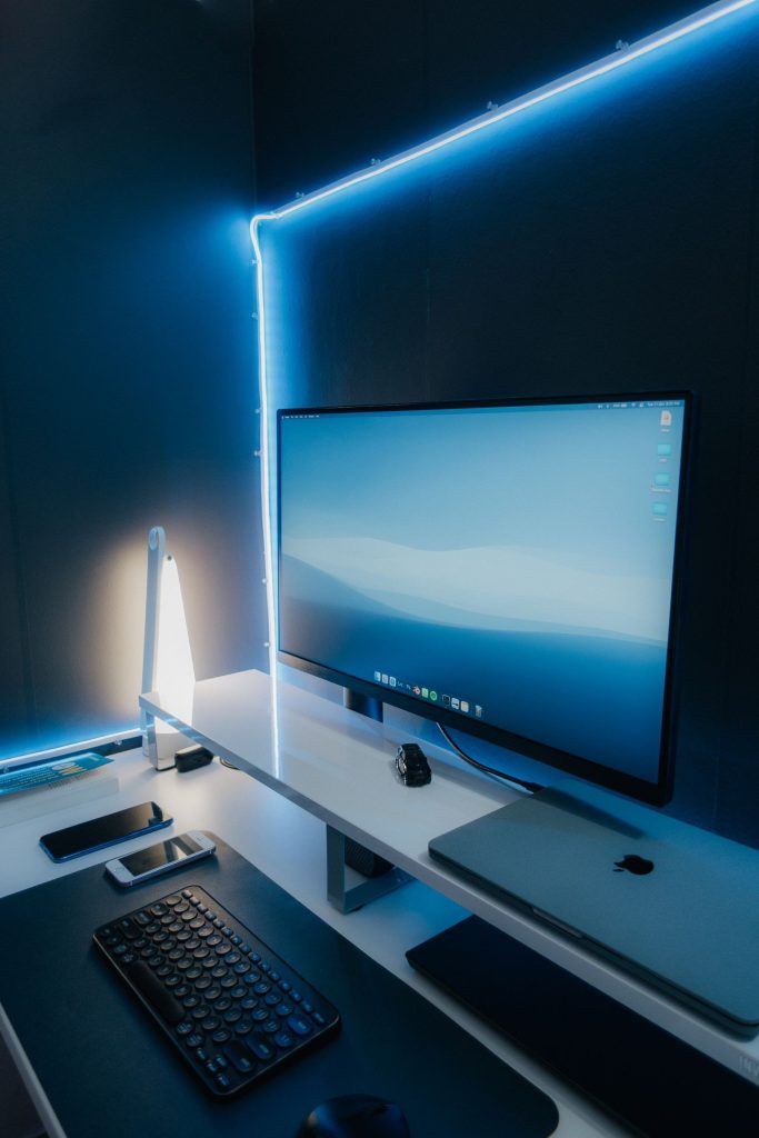 Poste de travail blanc avec écran et clavier installé dans un coin de pièce, sous un éclairage LED bleu