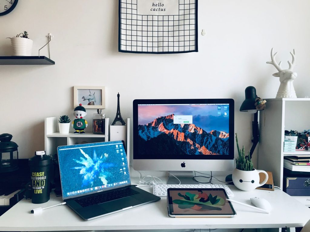 Poste de travail blanc avec un écran, un ordinateur portable et des étagères décorées