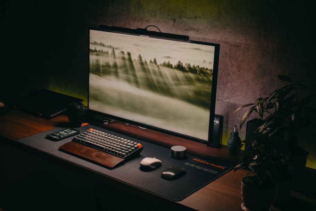 Poste de travail épuré avec écran, barre lumineuse, clavier sur repose-poignets et sous-main noir, sans câble apparent